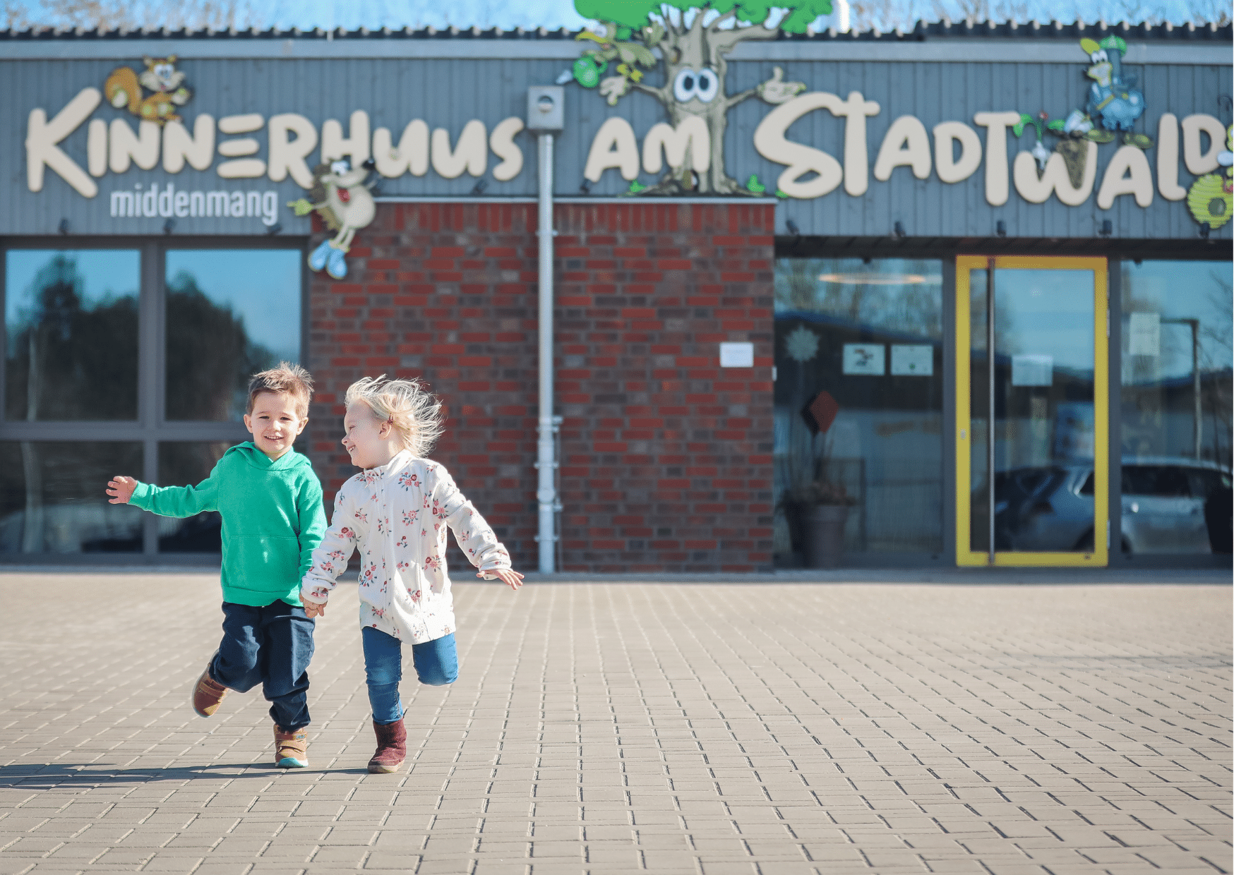 zwei Kinder laufen vor der Kita auf die Kamera zu