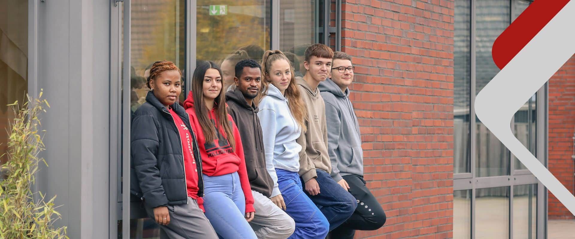 eine Gruppe junger Menschen lehnt an einer Mauer
