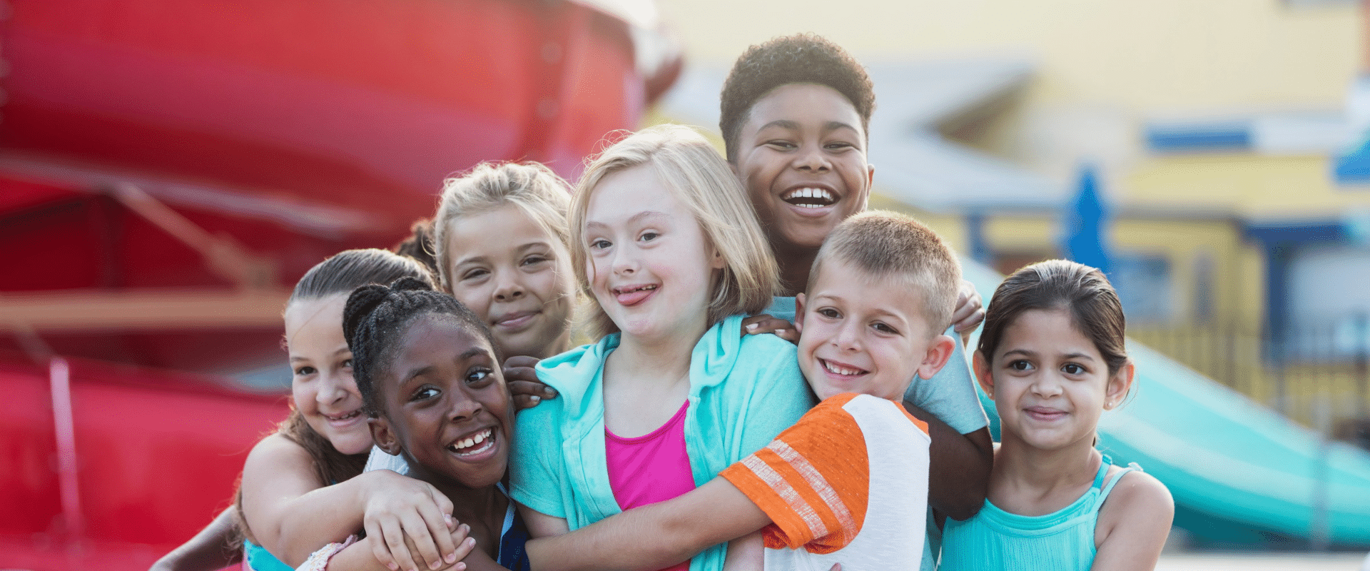 Ein Mädchen mit Down-Syndrom wird von einer Gruppe Kinder umarmt.