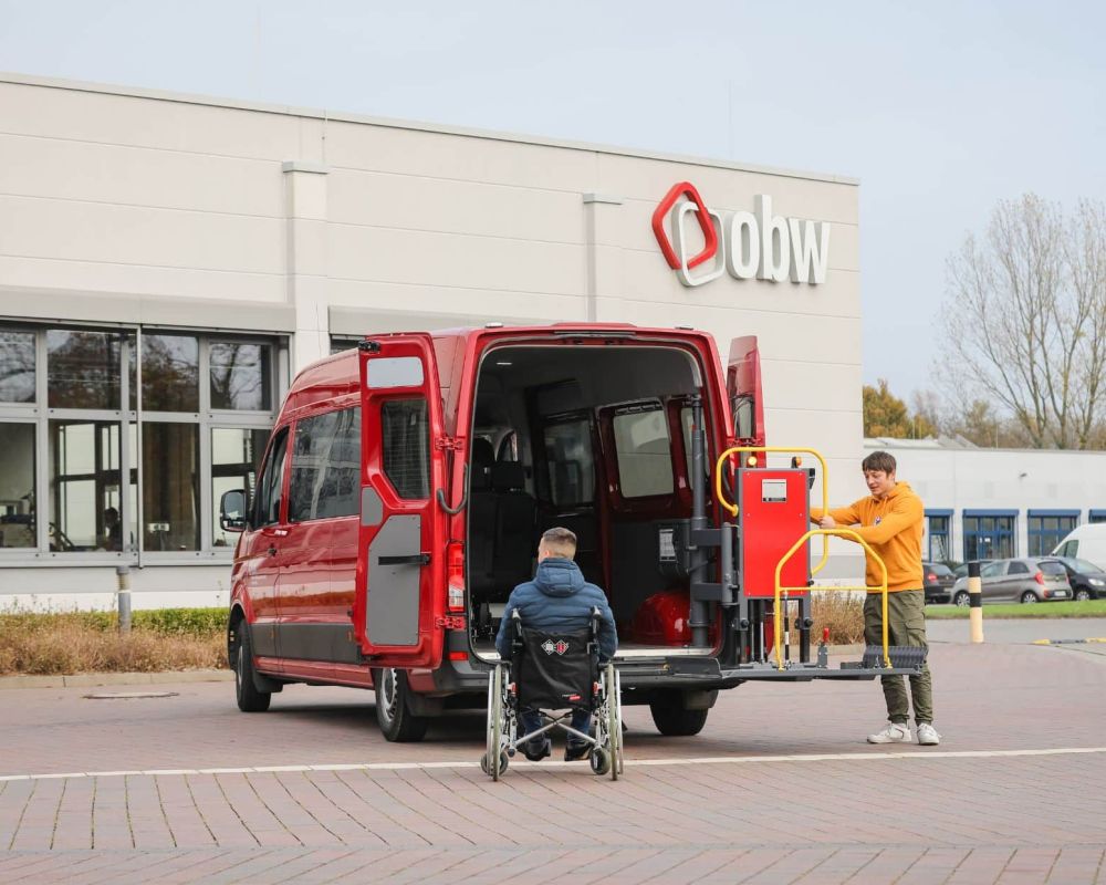 Freiwilliger unterstützt Rollstuhlfahrer beim Einsteigen in einen PKW