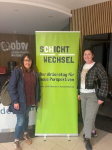 Zwei Frauen stehen vor einem Roll-Up zum Schichtwechsel